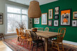 © Muhammad ibrahim - A warm, eclectic dining room with mismatched vintage chairs surrounding a rustic wooden table. The walls are painted a deep emerald green, and the room is filled with gallery wall art in a variety of