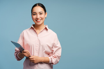 Smiling Asian businesswoman holding digital tablet smiling, looking at camera on blue background
