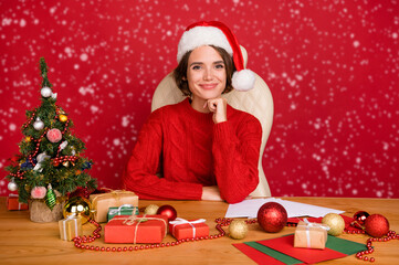 Wall Mural - Photo portrait young woman smiling sitting at table in headwear isolated bright red color background