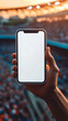 © Michael - Person in a crowded stadium at sunset is holding a smartphone with a blank screen while watching a sports event
