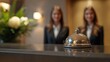 © CinimaticWorks - closeup of a hotel service bell on the reception desk, with two professional women in suits in the background, representing the luxury hotel’s hospitality and guest services at the front desk