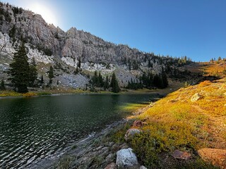 Sunrise on High Creek Lake with grey rock cliffs and pine trees reflecting in the alpine clear water in the fall in northern Utah 