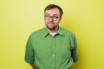 Casual portrait of a man wearing glasses and a green shirt, standing against a vibrant yellow background, showcasing a playful and thoughtful expression in a colorful setting.