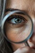 © Un_Un - A close-up of a woman eye looking through a magnifying glass, highlighting the detailed wrinkles under the eyes. Generative AI