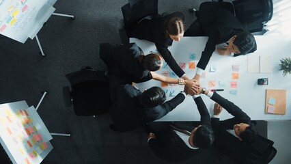 Top down aerial view of professional investor team putting hand together. Skilled diverse business team to celebrate successful project at meeting table with sticky note. Love and unity. Directorate.