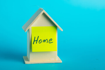 Wooden house model with yellow home note on blue background