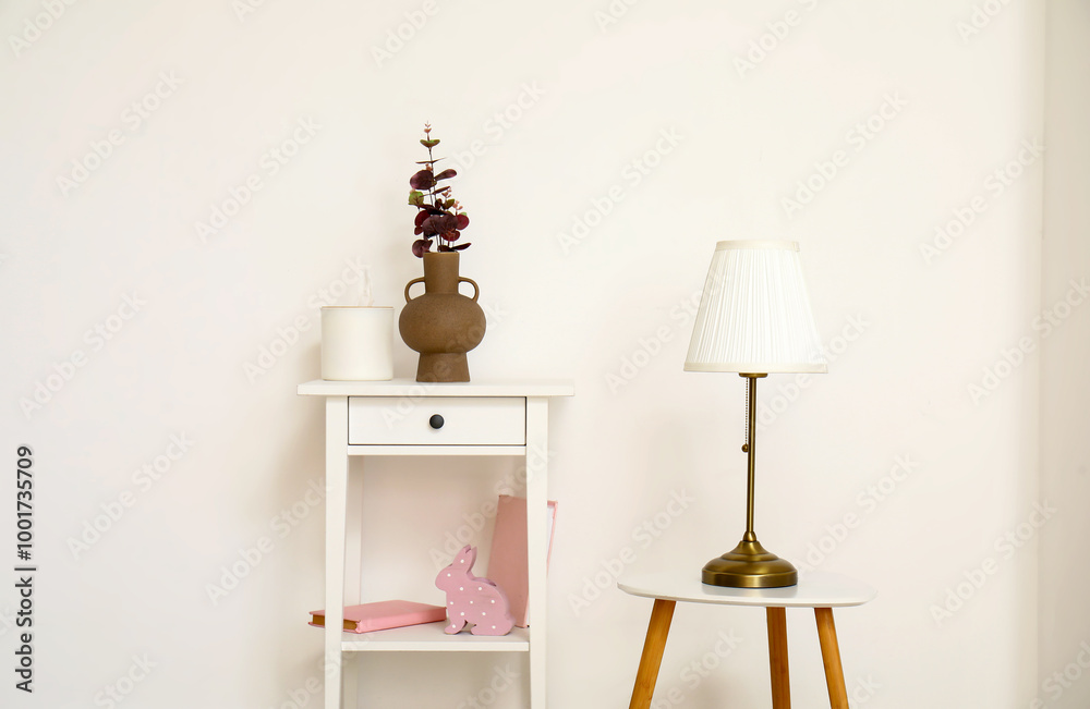 Vase with eucalyptus branches on dressing table and lamp near white wall