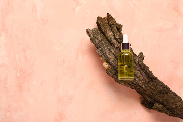 Wall Mural - Bottle of cosmetic oil with tree bark on pink background