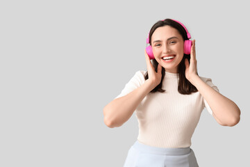 Wall Mural - Smiling young woman in headphones on grey background