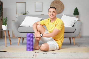 Wall Mural - Sporty young man with foam roller sitting at home