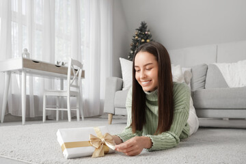 Poster - Happy young woman with Christmas gift box lying on floor at home