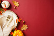 © photoguns - Autumn table setting with white plate, gold cutlery, beige napkin, and decorations of pumpkins, acorns, and fall branches on a deep red background. Thanksgiving dinner concept.