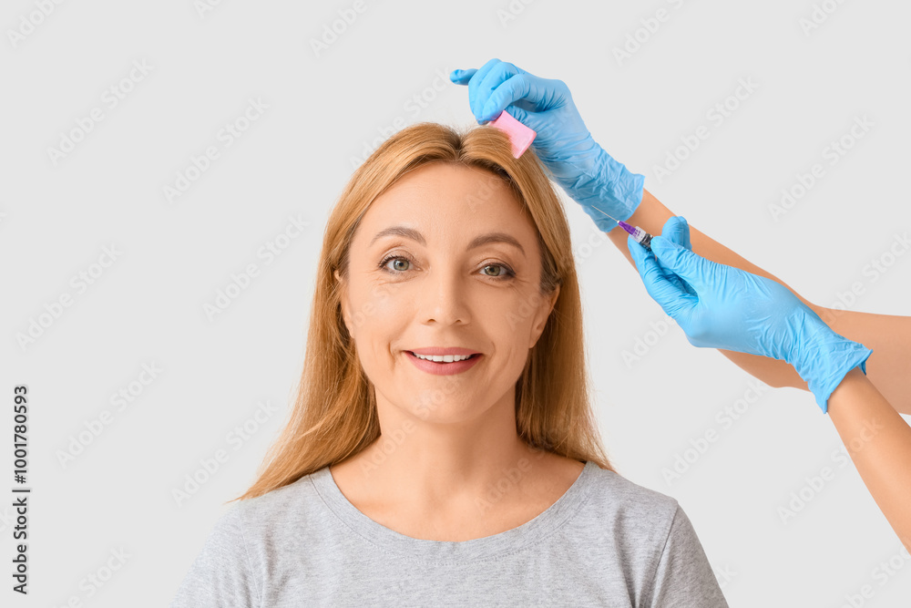 Mature woman with hair loss problem receiving injection on light background