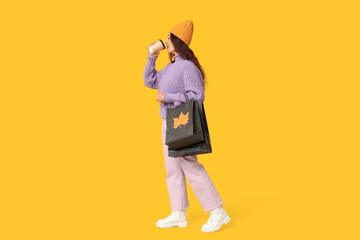 Wall Mural - Beautiful young Asian woman with shopping bags and paper cup of coffee on yellow background