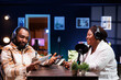 © DC Studio - African American podcast host interviews a female content creator in a neon-lit home studio using advanced recording equipment. Their engaging discussion is broadcast digitally to their online fans.