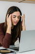 © Xavier Lorenzo - Young adult woman suffering from a headache or migraine due to looking at laptop screen while working at home. Vertical photo.