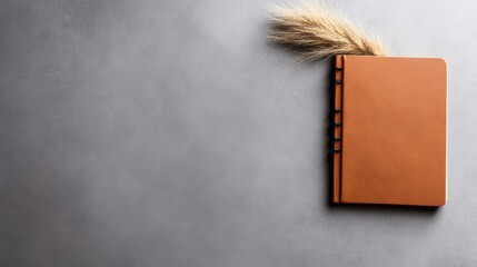 Poster - a small, brown notebook sits diagonally on a soft gray surface, elegantly paired with a single pampa