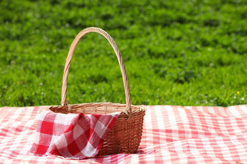 Sticker - One picnic wicker basket with checkered napkin and blanket on green grass. Space for text