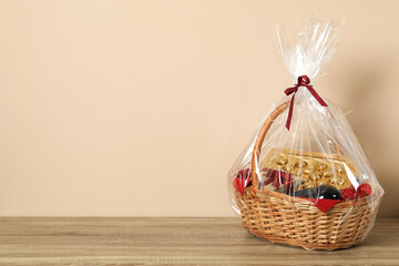 Canvas Print - Wicker gift basket on wooden table against beige background. Space for text