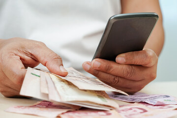 Asian woman counting Thai baht banknote money and holding smartphone, investment economy, accounting business and banking.