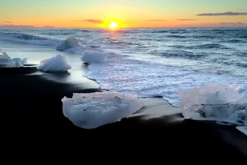 Sticker - . Sunset casts a warm glow on icebergs scattered across a black sand beach, creating a striking contrast.