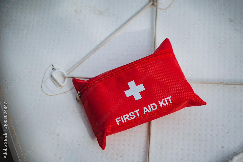 The first aid kit is red in color and prominently features a white ...