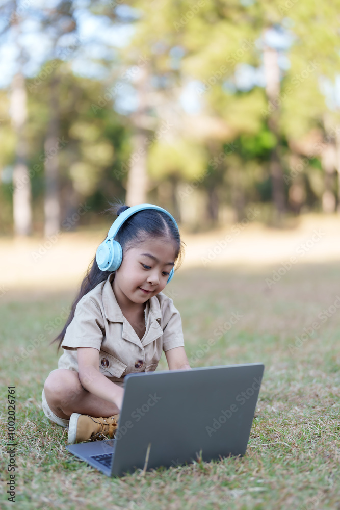 Asian girl sitting on grass in a national park using a laptop. Girl ...
