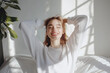 © piyacm - A young woman relaxing in bed with a serene smile, enjoying a peaceful morning at home