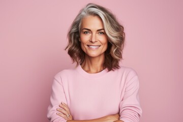 happy mature woman with folded arms looking at camera and smiling while standing against pink backgr