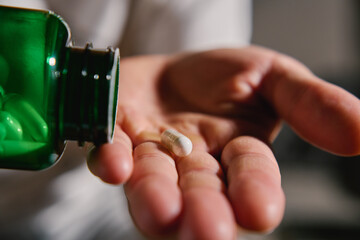 Close-up of man pouring white capsules from green bottle into hand. Person is taking pills or vitamins. Concept of supplements, medicine or health care