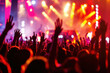 © oksa_studio - concert scene with a crowd raising hands under colorful stage lights, capturing the energy of live music.