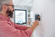 © Halfpoint - Man using smart thermostat, adjusting, lowering heating temperature at home. Concept of sustainable, efficient, and smart technology in home heating and thermostats.