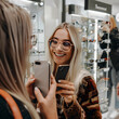 © mindstorm - Happy woman trying new eyeglasses taking selfie with friend in optics store