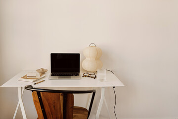 Contemporary work environment with laptop, notebooks, and paper lamp on sleek white desk