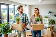© Yauhen - New home owners with boxes and indoor plants in their hands, rear view. A married couple takes things to another rented bright apartment. Home ownership in a mortgaged apartment. The beginning of a ha