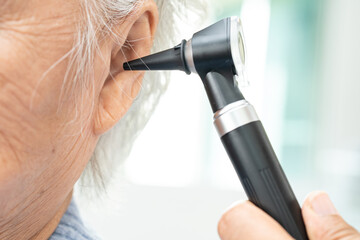 Audiologist or ENT doctor use otoscope checking ear of asian senior woman patient treating hearing loss problem.