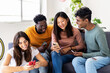 © Xavier Lorenzo - Diverse group of young student friends having fun using mobile phones at home. Millennial people watching social media content on smart phone app relaxing on sofa