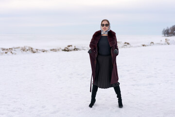 Wall Mural - A woman is standing in the snow wearing a black skirt and a red coat