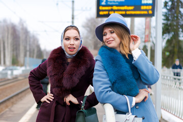 Wall Mural - Two women wearing fur coats and hats are standing on a train platform