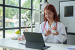© Phimwilai - Female doctor holds a brain model medical consultation While the doctor is writing on the clipboard Explain online via laptop to patients, education, care concepts, treatment, health insurance.