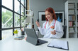 © Phimwilai - Female doctor holds a brain model medical consultation While the doctor is writing on the clipboard Explain online via laptop to patients, education, care concepts, treatment, health insurance.