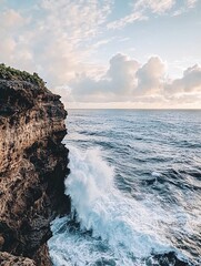 Wall Mural - Dramatic waves crashing against a rocky cliff face, with a blue sky and fluffy clouds in the background.