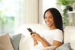 © Antonioguillem - Happy black woman holding cell phone looking at you at home
