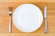 © JP STUDIO LAB - A simple white plate on a minimalist wooden table, with a knife and fork neatly placed beside it