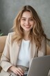 © Andrii Zastrozhnov - A woman is sitting in a chair with a laptop in front of her. She is wearing a tan jacket and a white shirt. She is smiling and she is happy