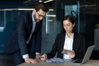 © Liubomir - Business professionals engaged in workplace discussion over project details. Woman uses tablet for reference. Man leans over table, emphasizing teamwork. Office environment highlights technology