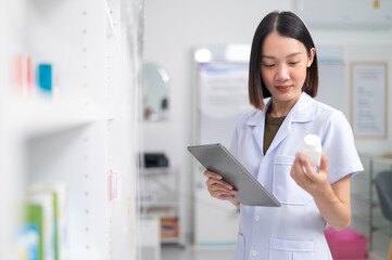 Wall Mural - Asian professional female pharmacist using tablet to check drug list Pharmacist checking stock in pharmacy for health medicine in technology pharmacy looking at camera smiling