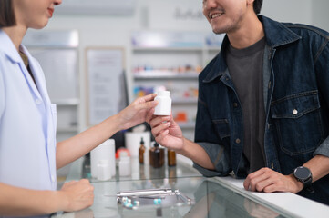 Wall Mural - Asian professional female pharmacist using a digital tablet computer to dispense prescription medication to male customers. The doctor advises and explains to the client about the medication.