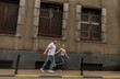 © Vasil - A couple is running down a street, with the man wearing a white shirt and jeans. The woman is wearing a striped shirt