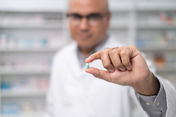 Wall Mural - Asian professional male pharmacist looking at camera charming smile pointing hand to pill bottle health care products in pharmacies Close-up and wide-angle shots